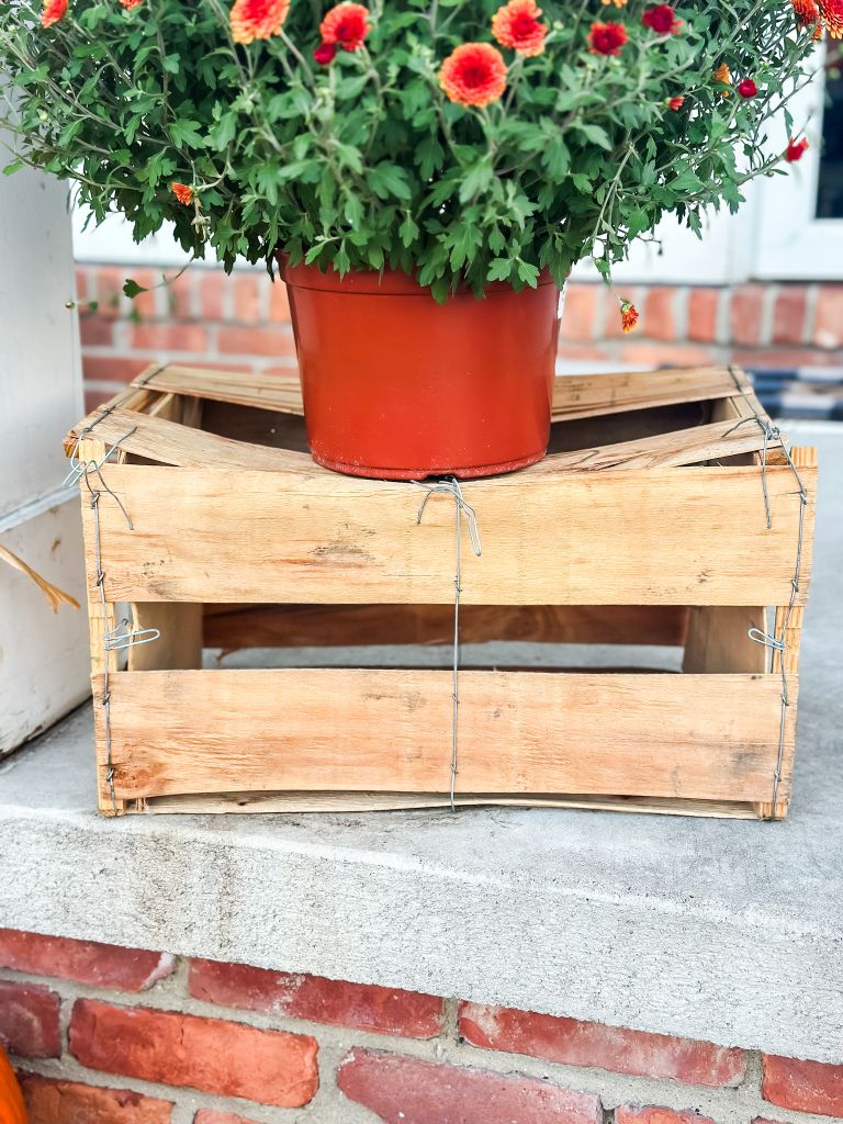 A planter of fall mums elevated on a salvaged wooden crate, a simple and inexpensive DIY idea for a cozy autumn porch.