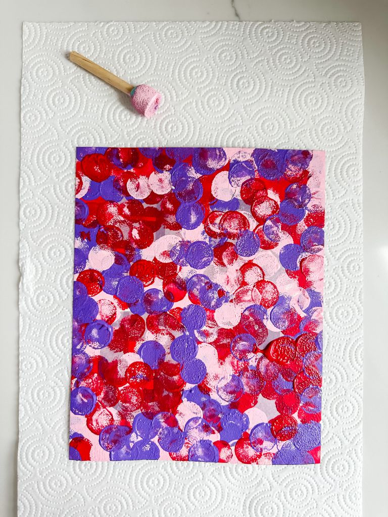 Canvas paper covered in pink, red, and purple paint dots using a sponge dauber for a Valentine's Day process art project.