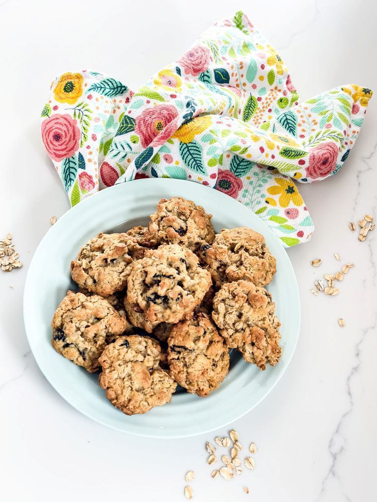 Freshly baked cherry oatmeal cookies, a Michigan-inspired treat, served on a blue plate with a vibrant floral napkin. A perfect 'something warm from the oven' for a cozy traditional cottage home.