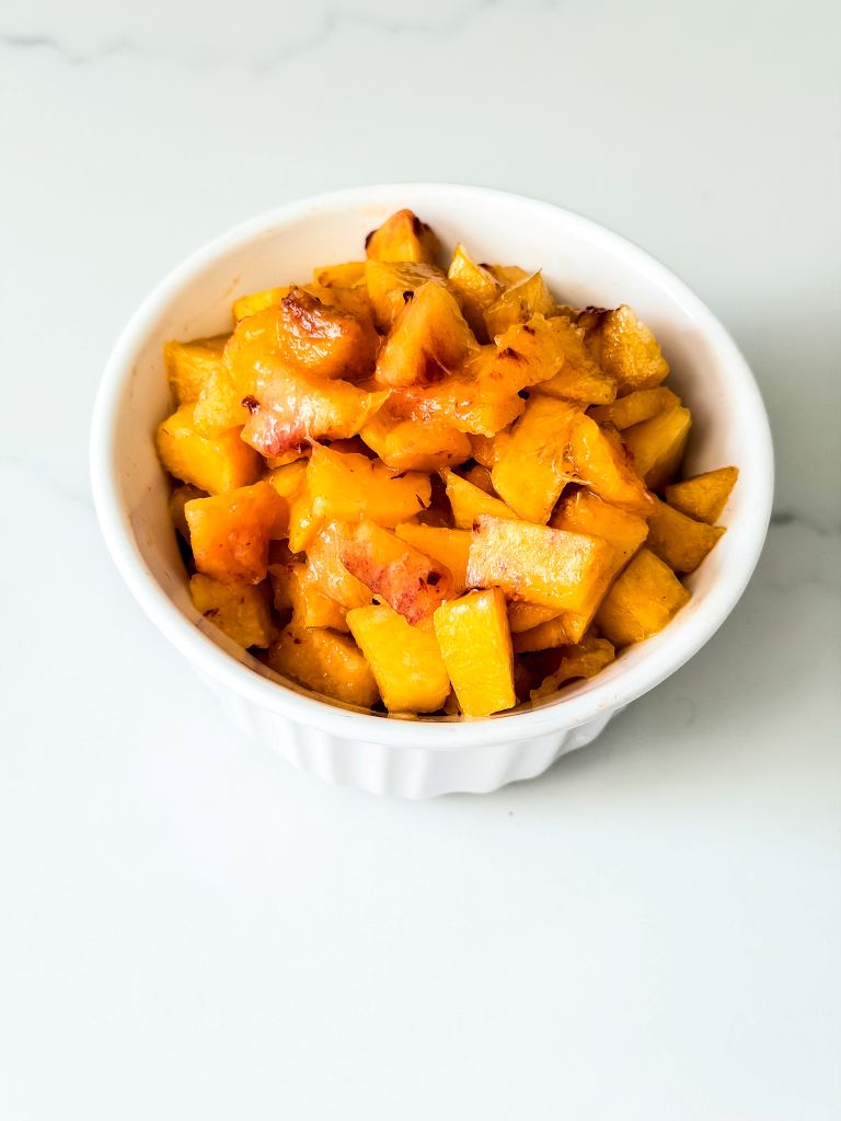 Small white fluted bowl packed with chopped juicy ripe peaches on a marble surface.