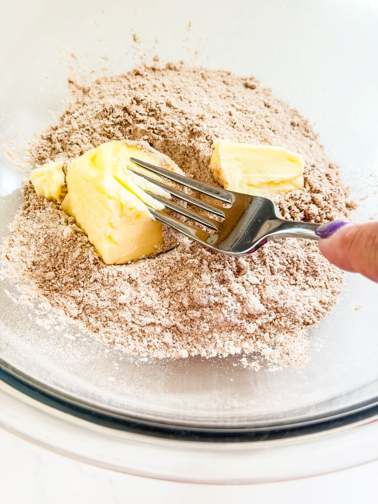 Cutting butter into flour and cinnamon with a fork to make a streusel crumble topping for peach muffins.