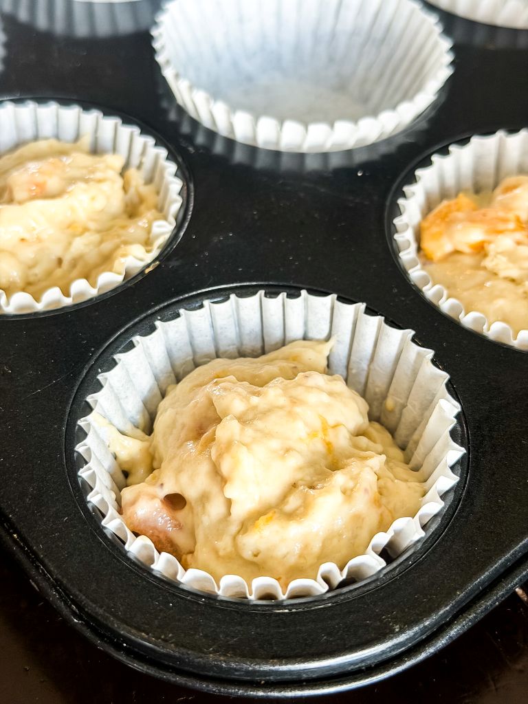 Raw peach muffin batter scooped into paper liners inside a black muffin pan before baking.