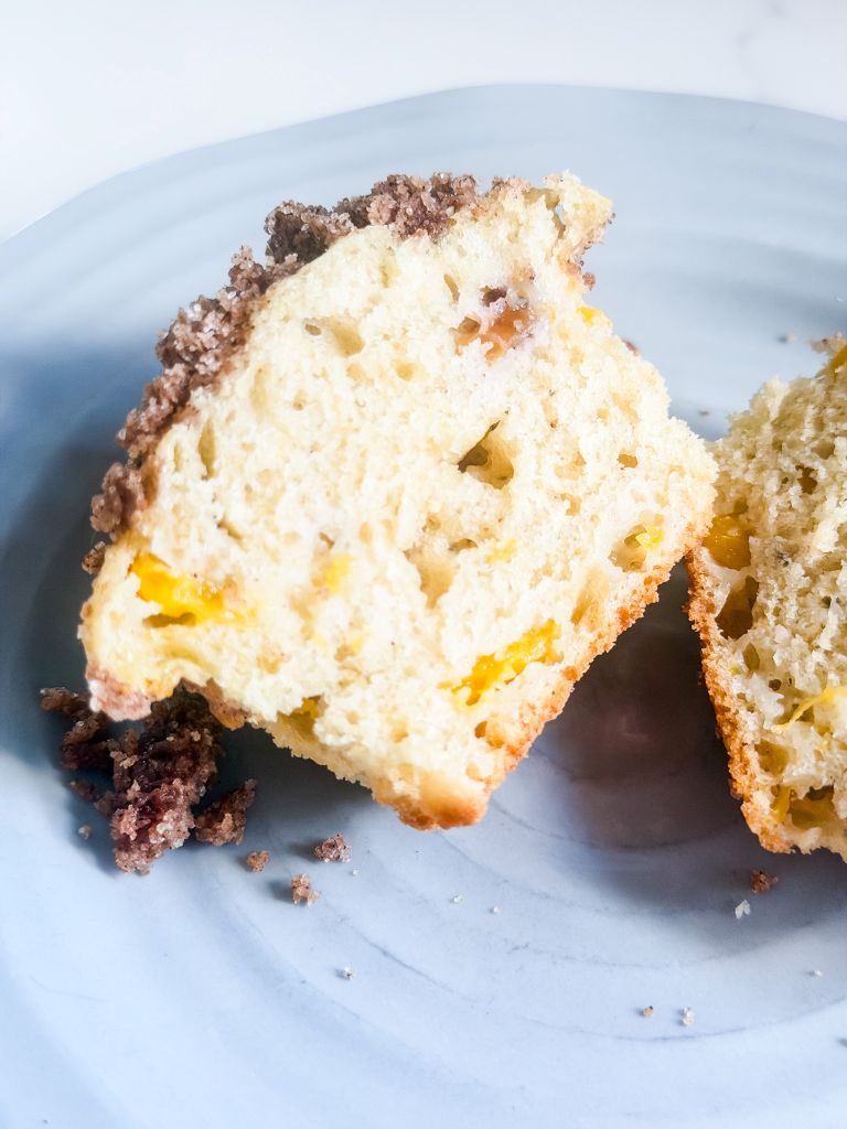 Fresh peach muffin cut in half on a blue plate showing the tender interior, real peach pieces, and cinnamon streusel crust.