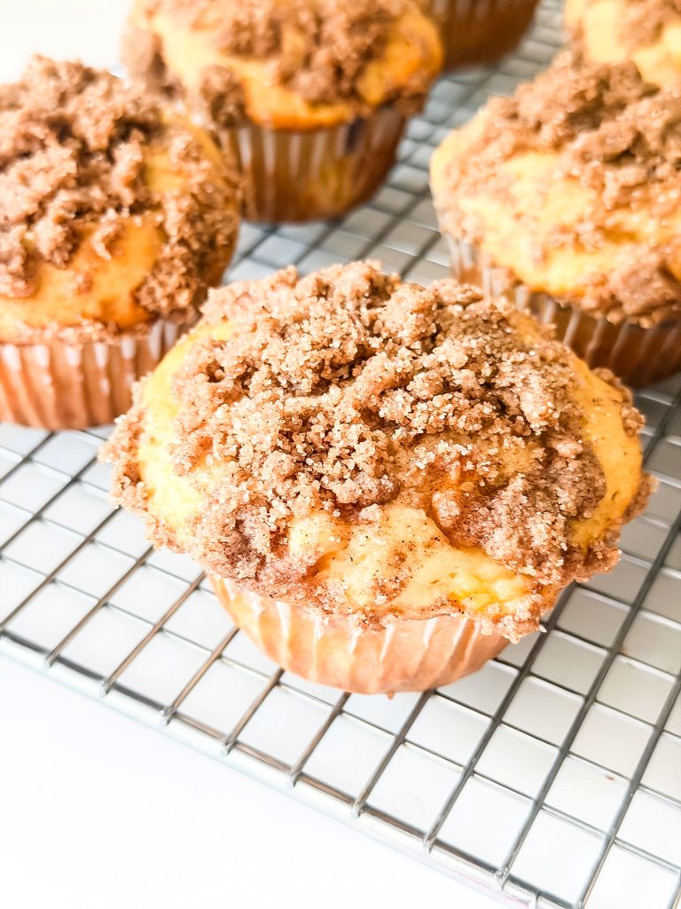 Freshly baked peach muffins with golden cinnamon crumble tops cooling on a wire rack.