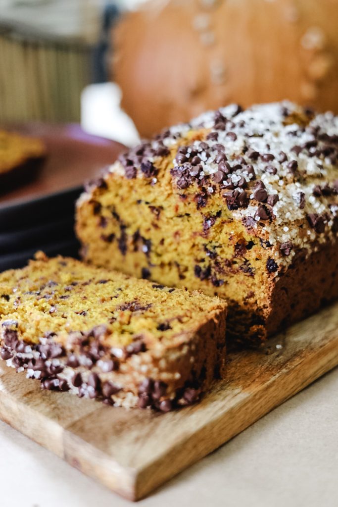 Sliced chocolate chip pumpkin bread on a wooden cutting board with warm autumn spices.