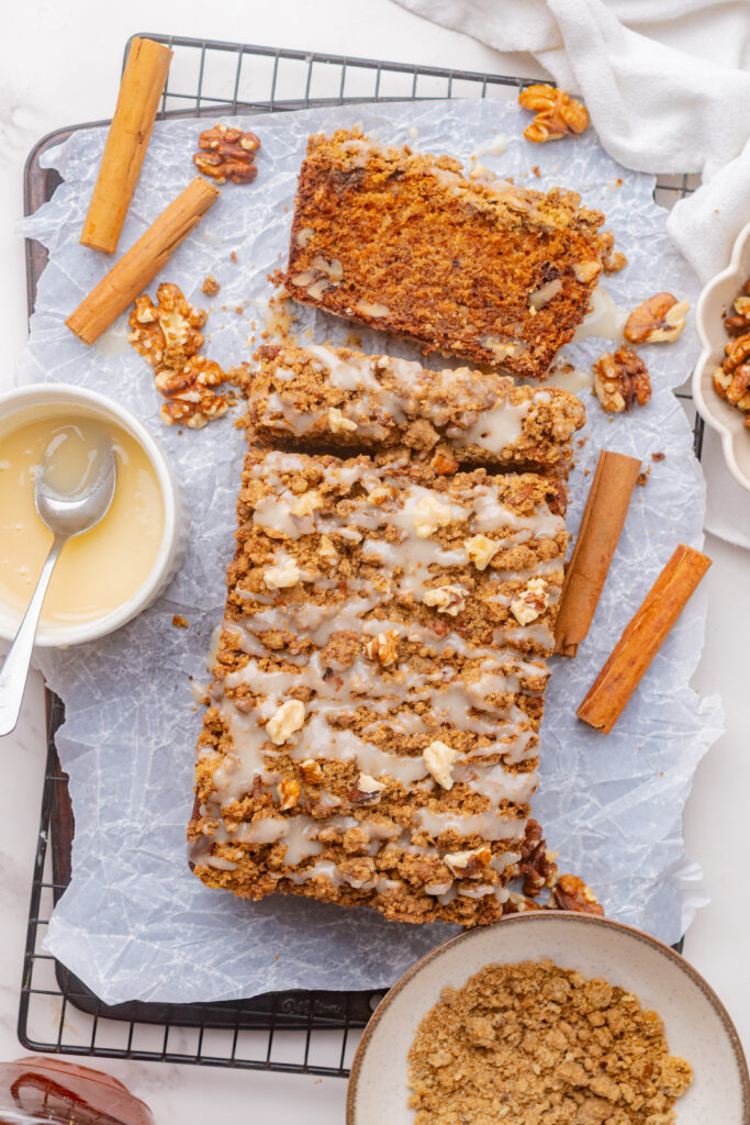 Sliced maple walnut loaf cake topped with sweet glaze and toasted nuts on a serving plate.