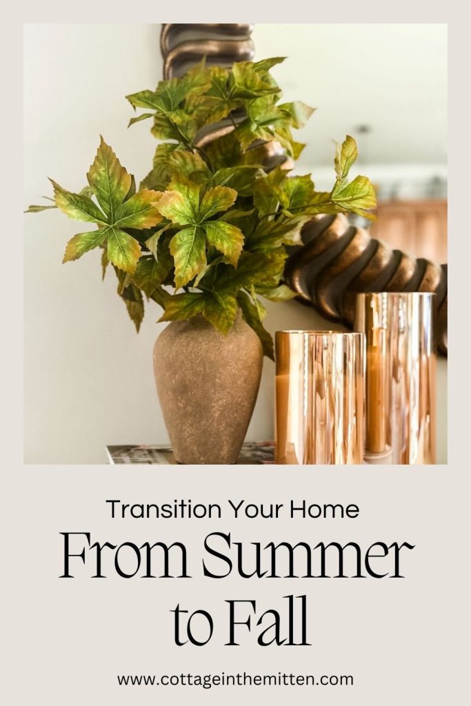 Pinterest pin for 'Transition Your Home From Summer to Fall' featuring a vase of green-and-gold faux fall leaves next to copper candle holders.